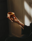 Person holding a coral TANO Cappuccino cup set in a minimalist and warm setting, emphasizing nordic style and timeless design.